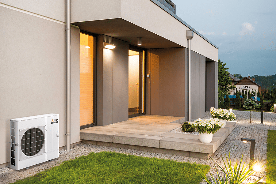 Mitsubishi Electric City Multi PUMY-SP compact outdoor air conditioner unit installed beside the entry of a modern home, showing suitability for residential applications