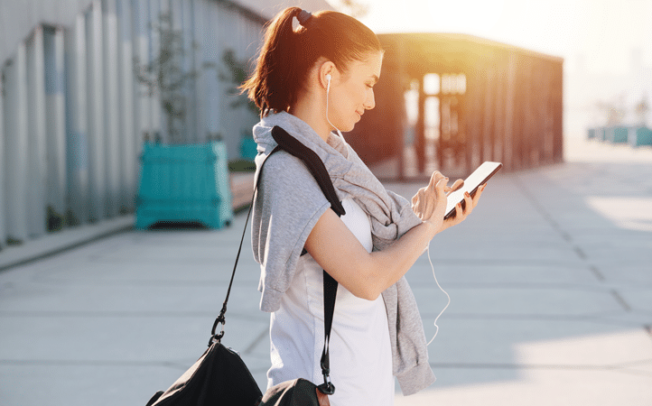 A person using a smartphone outdoors with earphones, likely adjusting her air conditioner settings remotely via a Wi-Fi enabled control app